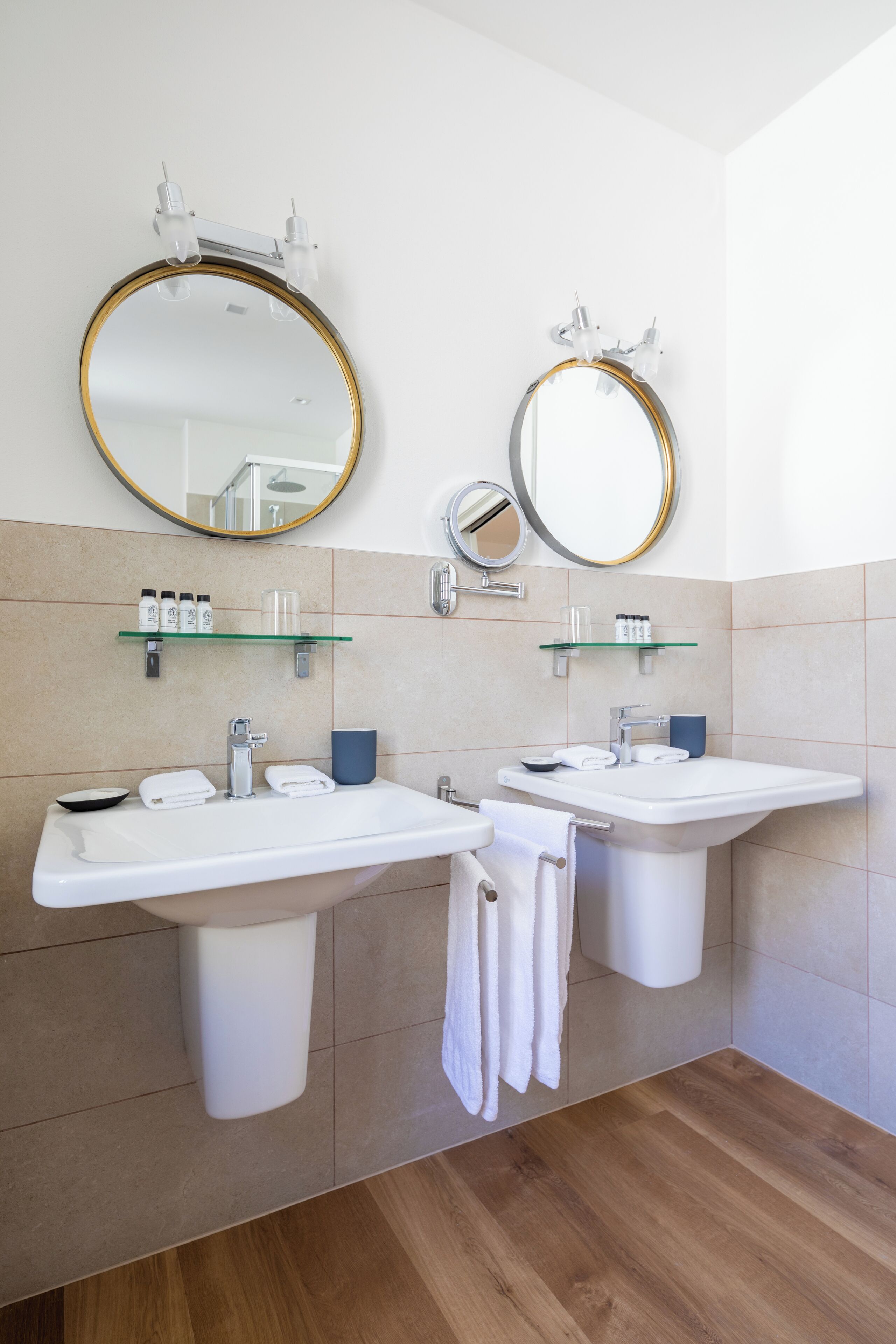 A modern bathroom with two sinks, a large mirror, and a glass shelf with toiletries.