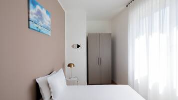 A bedroom with a bed, a nightstand, a lamp, a wardrobe, and a painting on the wall.