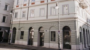 A multi-story hotel with a classic architectural style, featuring a symmetrical facade, multiple windows, and a ground-level entrance with a glass door. - Hotel Vis a Vis (Trieste)