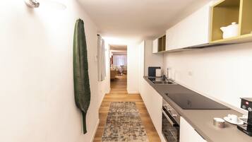 A narrow hallway with a kitchen on the right, a dining area in the background, and a patterned rug on the floor.
