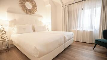 A large bed with white bedding, a round mirror above it, and a green chair to the right.