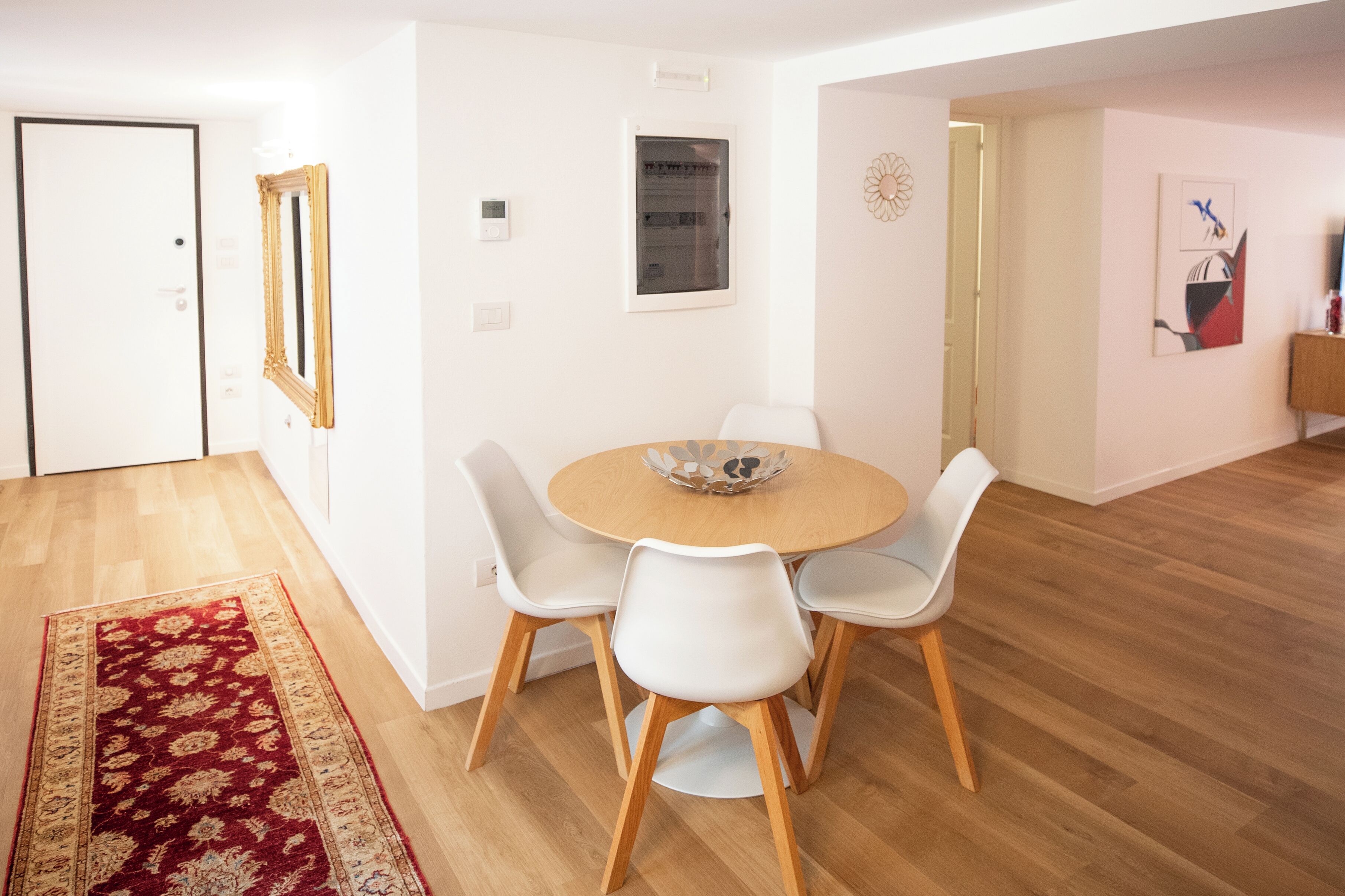 A dining area with a round table, white chairs, and a wooden floor.