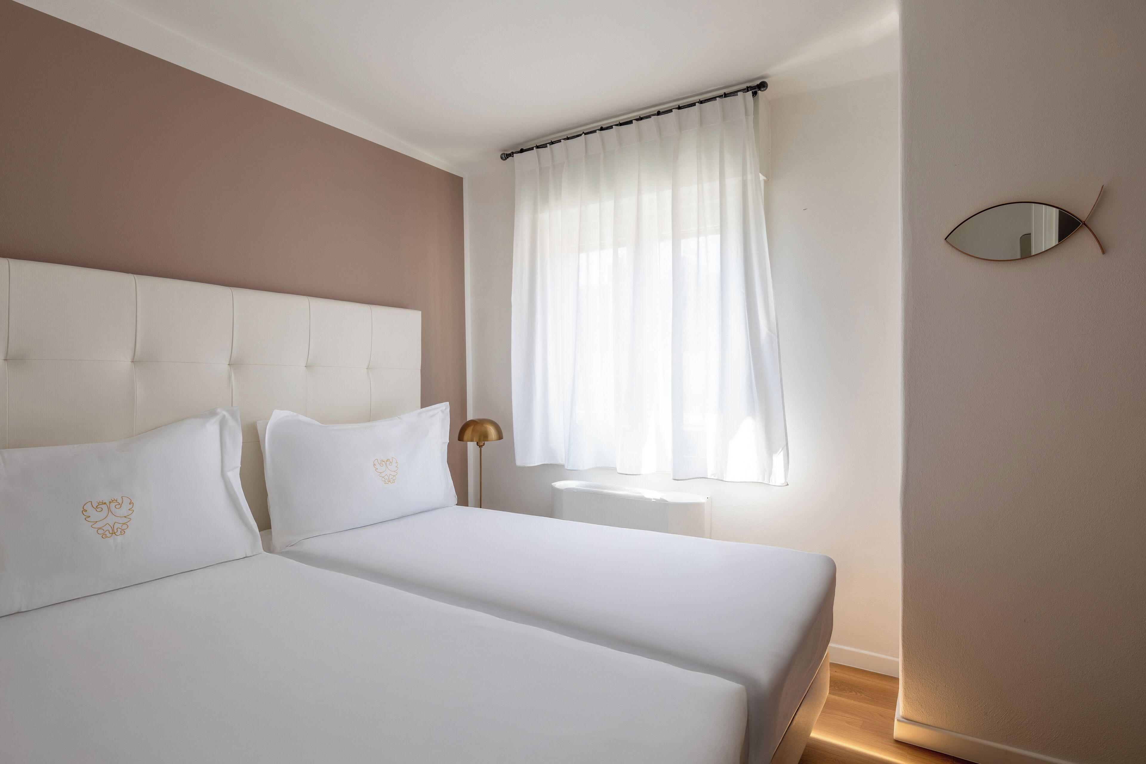Una camera da letto con due letti, un comodino, una lampada e una finestra con tende.