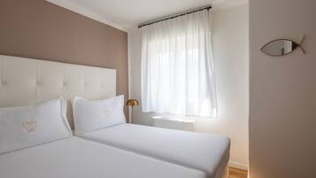 Una camera da letto con due letti, un comodino, una lampada e una finestra con tende.