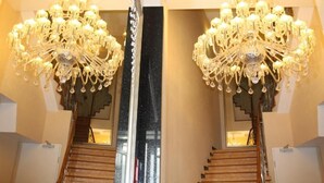 A grand staircase with a mirrored effect, flanked by two large, ornate chandeliers. - Hotel Expo Frankfurt City Centre - Digital Check-In (Frankfurt)