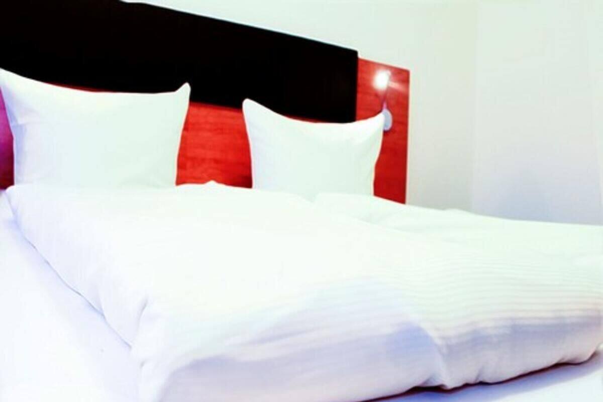 A neatly made bed with white linens and a red headboard.