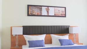 A hotel room with a bed, two bedside lamps, a headboard, and a framed picture on the wall. - Hotel Expo Frankfurt City Centre - Digital Check-In (Frankfurt)