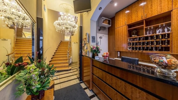 A hotel lobby with a wooden reception desk, a chandelier, a staircase, and a display of trophies. - Hotel Expo Frankfurt City Centre - Digital Check-In (Frankfurt)