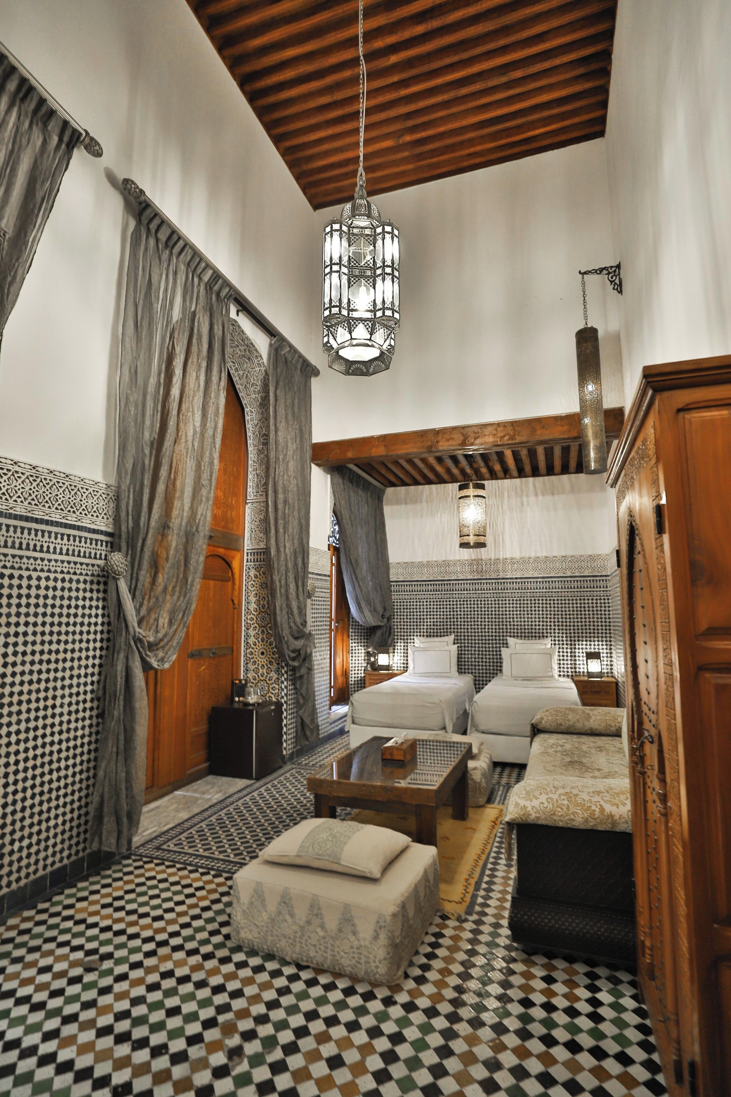 A traditional Moroccan interior with a checkered floor, wooden furniture, and a hanging chandelier.