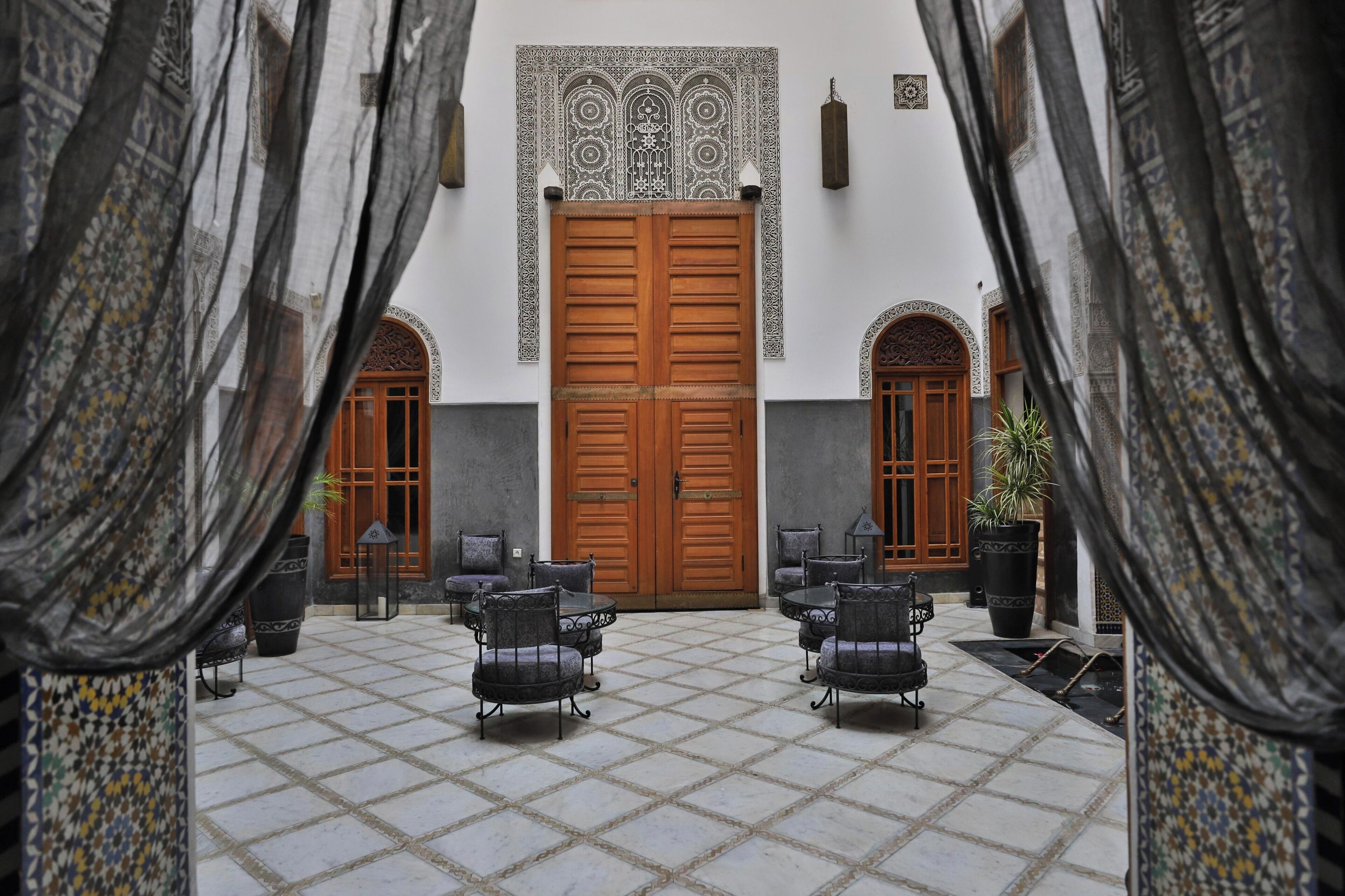 A courtyard with a tiled floor, two wooden doors, and four chairs arranged in a semi-circle.