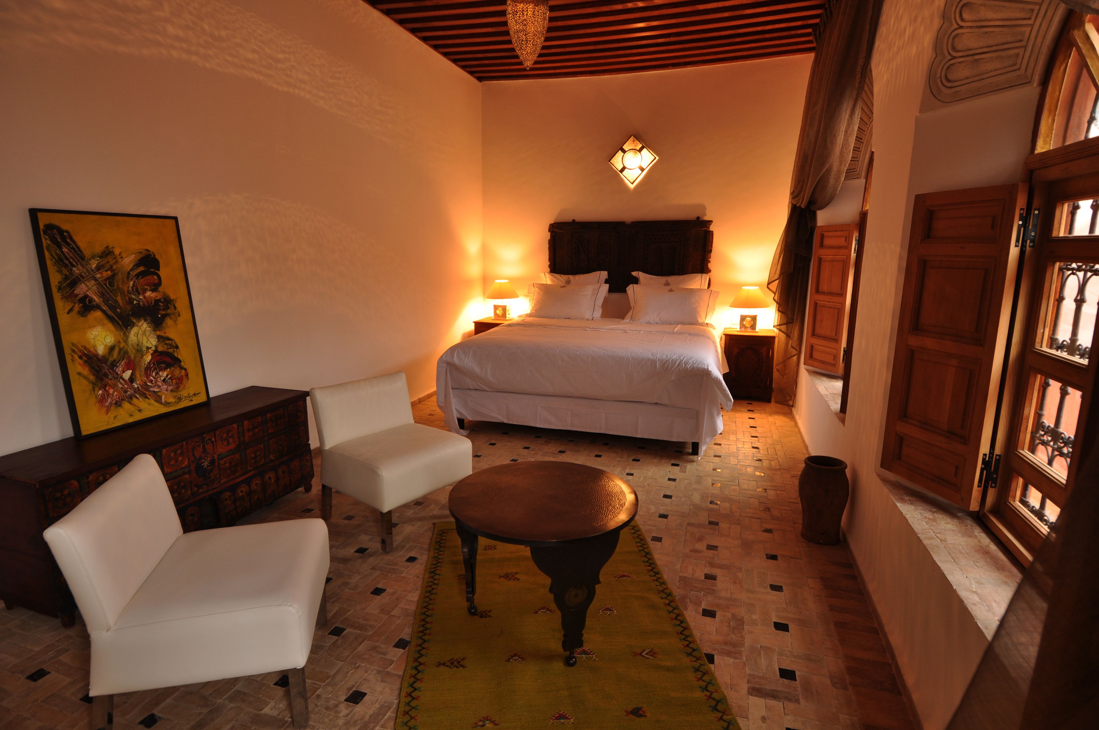 Un dormitorio con cama, mesitas de noche, una silla, un tapete decorativo y un cuadro en la pared.