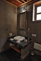 Um banheiro com piso quadriculado em preto e branco, pia branca, espelho e uma pequena prateleira com produtos de higiene pessoal.