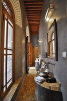 Um corredor estreito com piso de ladrilho de pedra, uma grande porta em arco e uma pia com toalha e um aparelho preto no balcão.