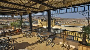 A terrace with outdoor seating, a view of the city, and decorative hanging lights. - Riad Layla (Fes)