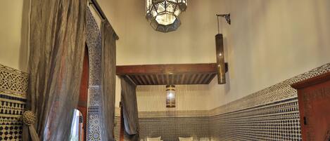 A traditional Moroccan interior with two beds, a sofa, patterned walls, and hanging lamps.