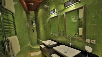 Un baño con paredes de azulejos verdes, dos lavamanos, una bañera y un espejo.