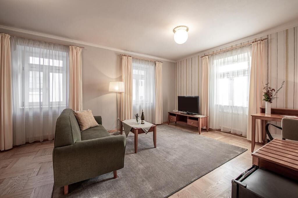 Ein Hotelzimmer mit einer Couch, einem Fernseher, einem kleinen Tisch mit einer Flasche und einer Lampe.