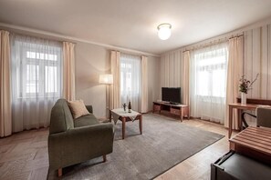 A hotel room with a sofa, a TV, a small table with a bottle, and a lamp. - Pension Krivá (Olomouc)