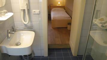 A compact hotel room with a bathroom, a bed, a bedside table with a lamp, and a telephone.