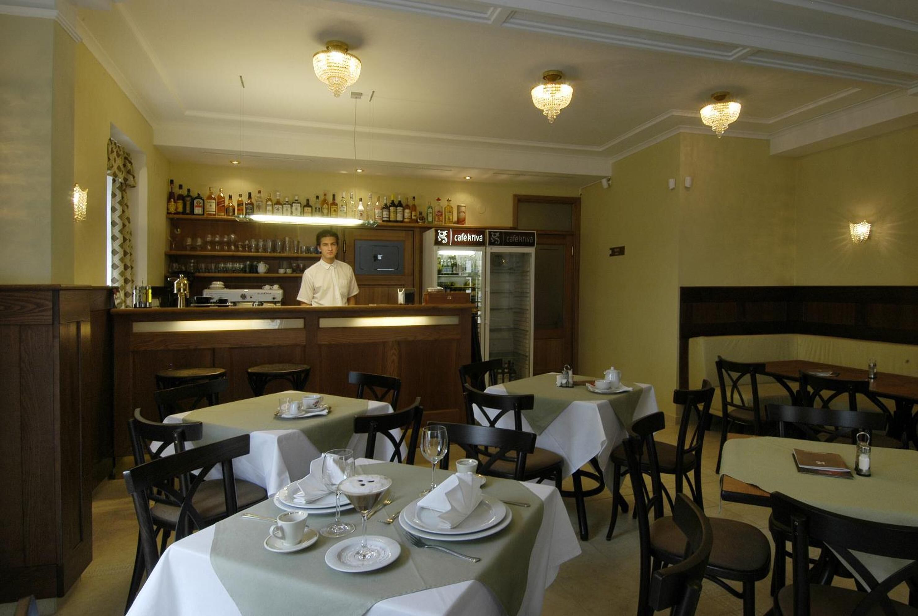 A restaurant with tables set for dining, a bar area with a bartender, and a refrigerator labeled 'cafe'.