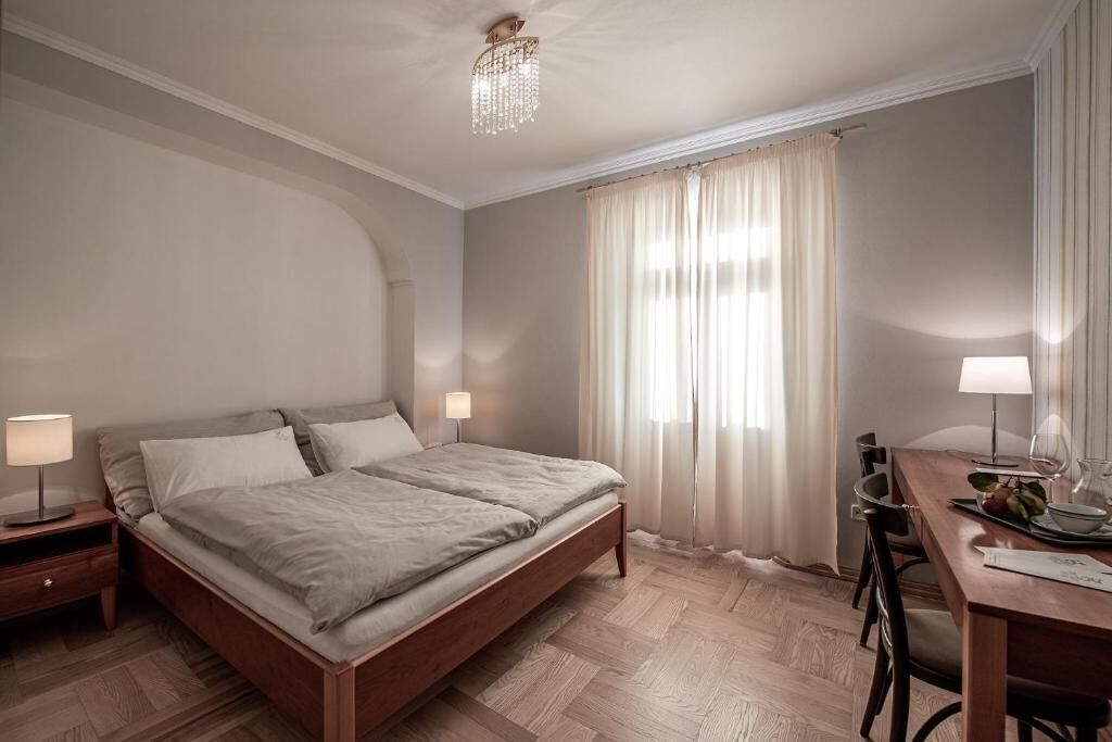 A bedroom with a bed, bedside tables, a desk with a chair, and a chandelier.
