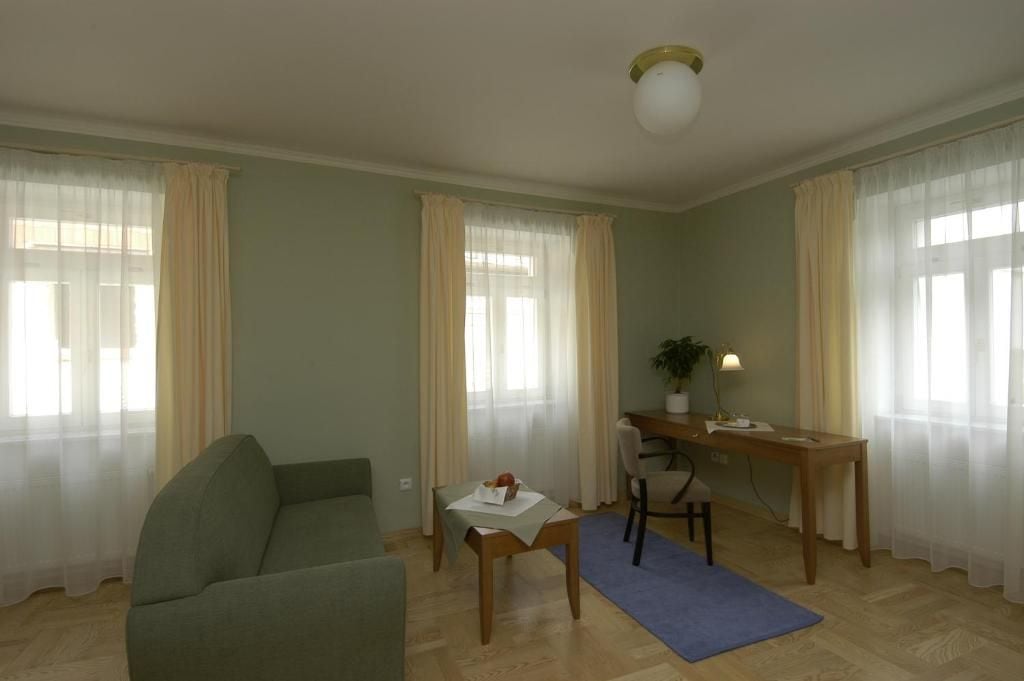 Ett vardagsrum med en soffa, ett matbord med stolar, ett litet bord med en växt och en blå matta.