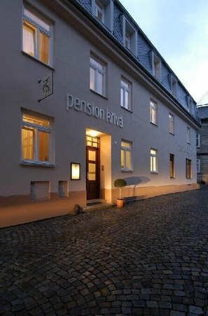 Un edificio con el letrero "pension Kriva" en la fachada, que presenta un estilo arquitectónico europeo tradicional y una calle adoquinada en primer plano.