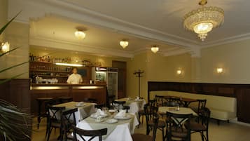 Un restaurante con varias mesas y sillas, una zona de bar y un candelabro.