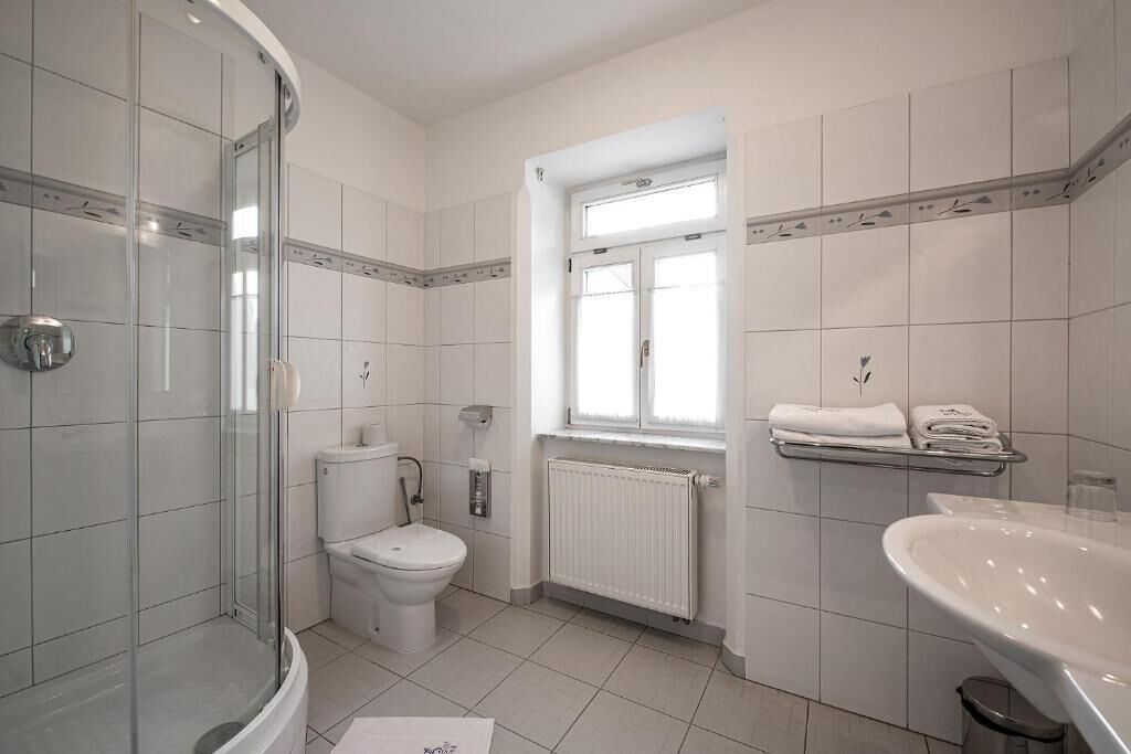 A bathroom with a glass-enclosed shower, a toilet, a radiator, and a sink.