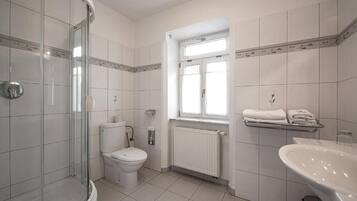 A bathroom with a glass-enclosed shower, a toilet, a radiator, and a sink.