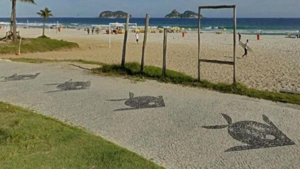 A beach with a paved walkway, palm trees, and a volleyball net. - Entremares Hotel (Rio de Janeiro)