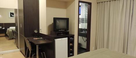 Una habitación de hotel con cama, escritorio con televisor, refrigerador pequeño y espejo.