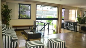 A lobby with striped sofas, a bench, a statue, and a staircase leading to a balcony with a view of the outside. - Entremares Hotel (Rio de Janeiro)