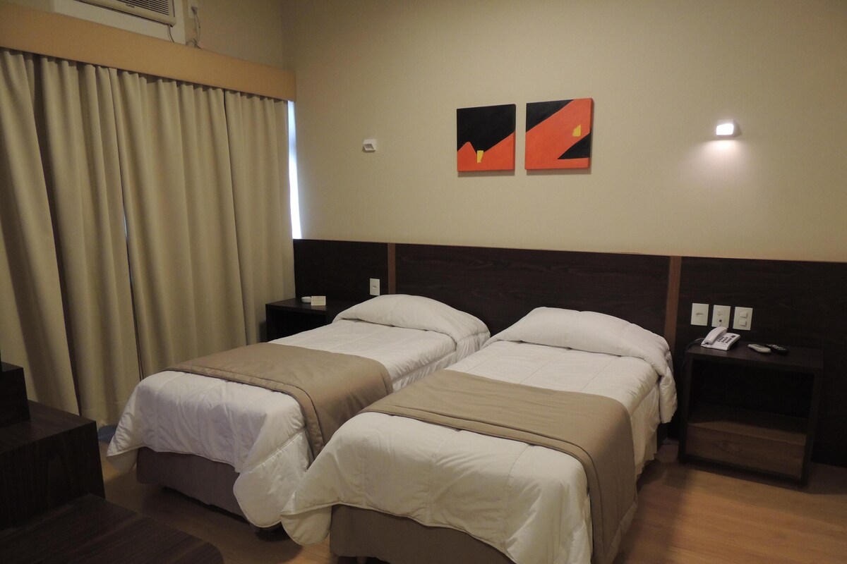 Une chambre d’hôtel avec deux lits, un bureau et une table de chevet équipée d’un téléphone et d’une télécommande.
