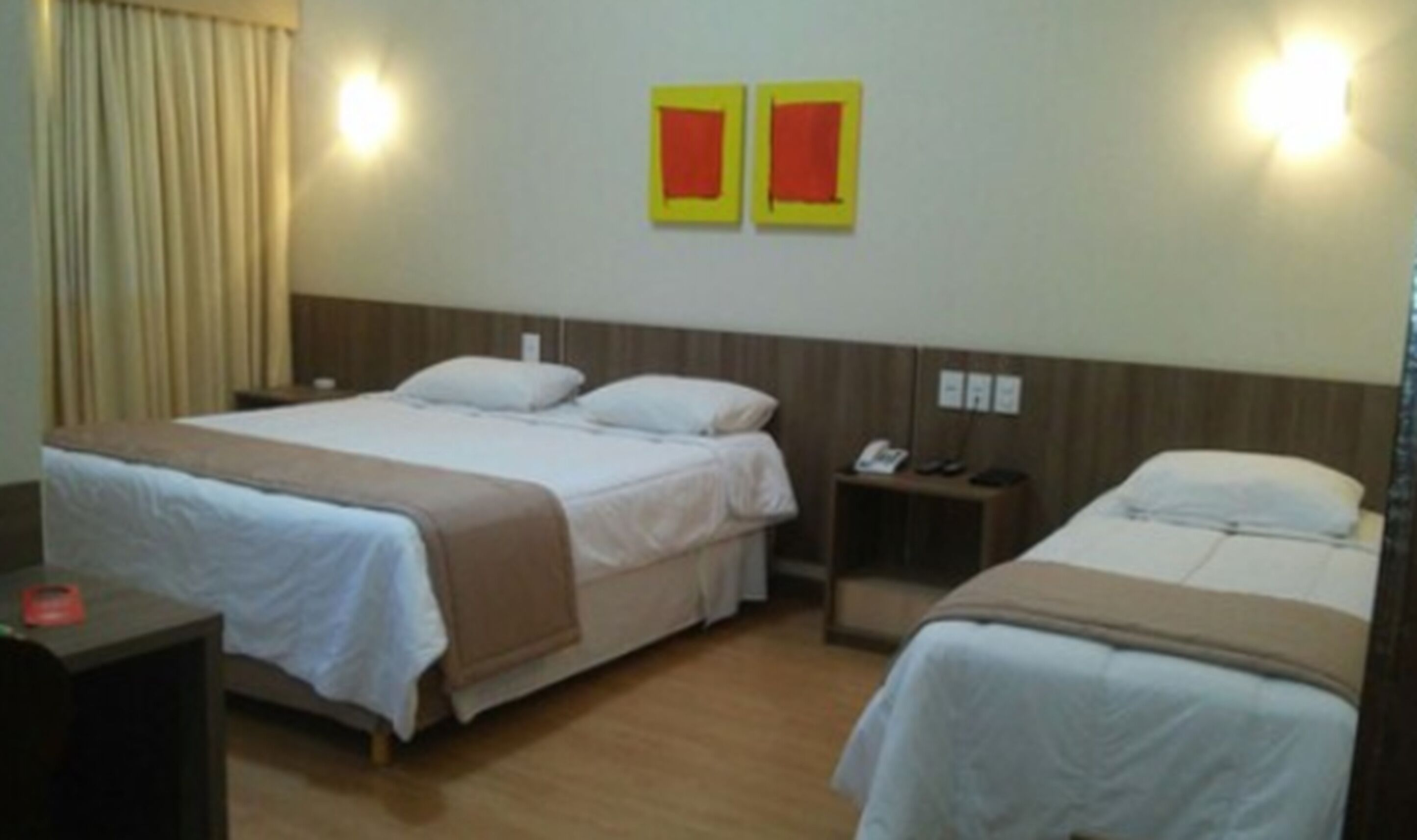 A hotel room with two beds, a wooden headboard, a nightstand with a phone, and a window with curtains.