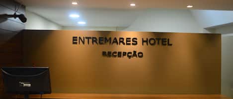 A reception area with a sign reading "ENTREMARES HOTEL RECEPCAO" and a computer monitor on a counter.