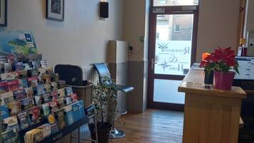 Una habitación con piso de madera, un escritorio con computadora, una silla, una planta y una exhibición de postales.