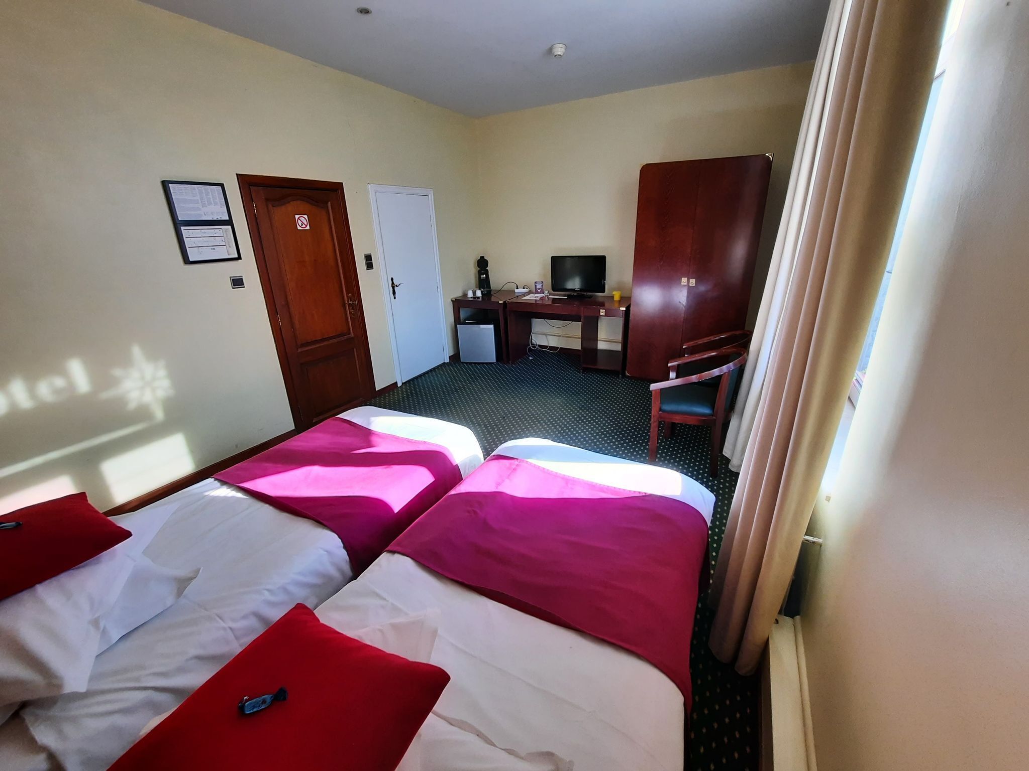 Ein Hotelzimmer mit zwei Betten, einem Schreibtisch, einem Fernseher und einer Tür.