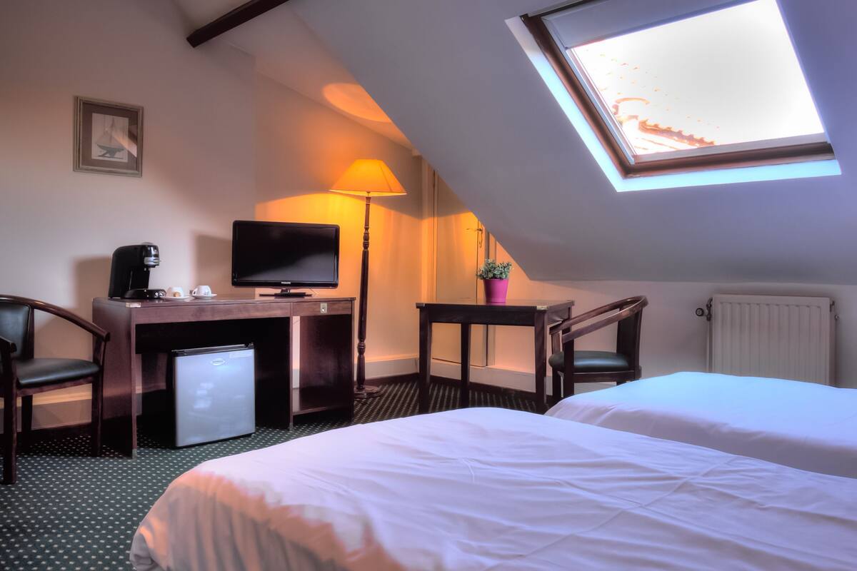 A hotel room with a bed, a desk with a computer, a chair, a coffee maker, and a small refrigerator.