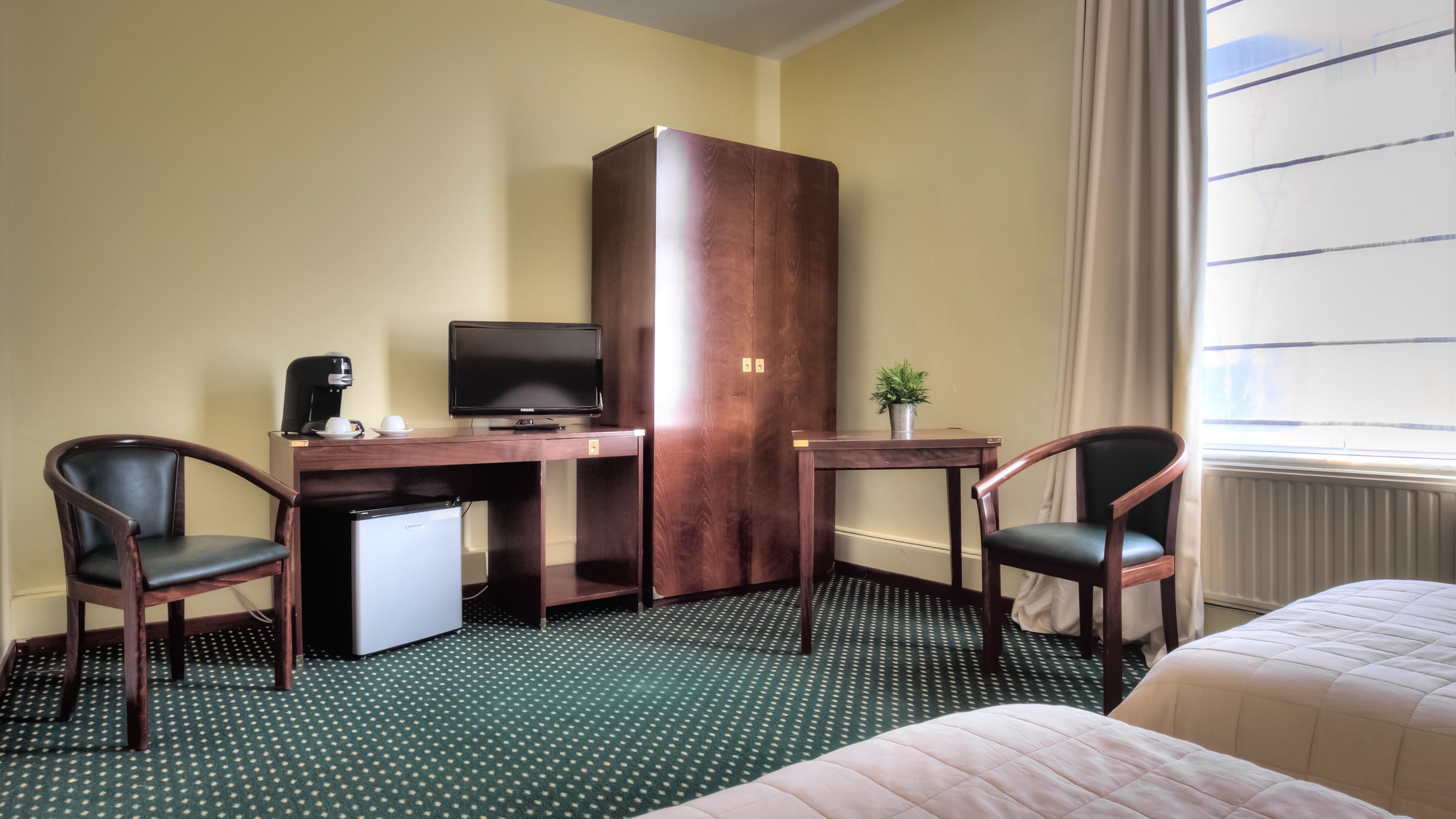 Een hotelkamer met een houten bureau, een televisie, twee stoelen, een kleine koelkast en een bed.