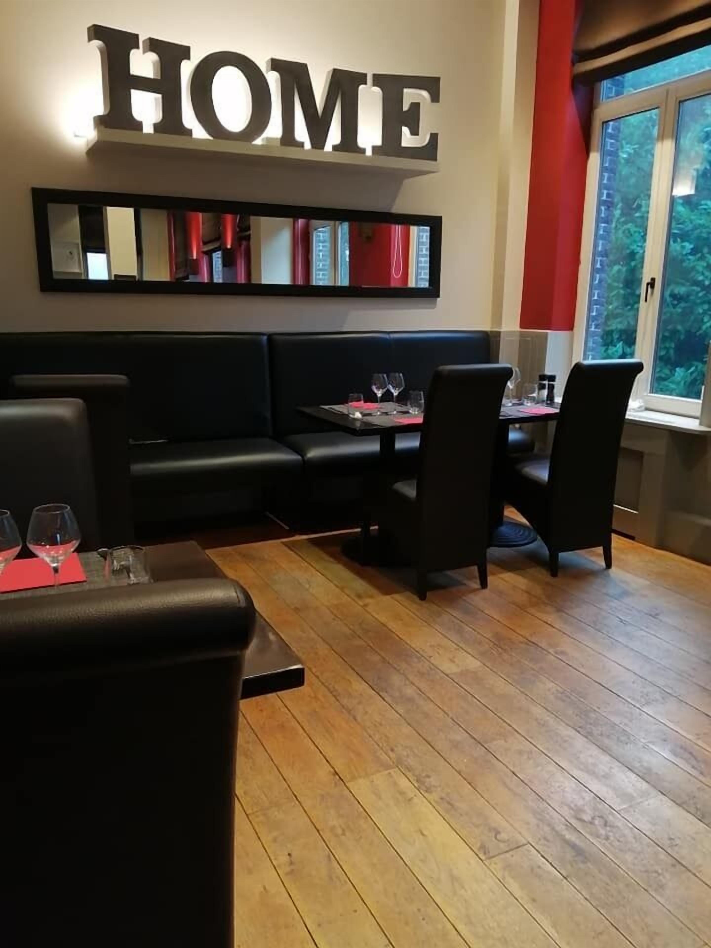 A cozy dining area with a 'HOME' sign, wooden flooring, black leather seating, and a window with a view.