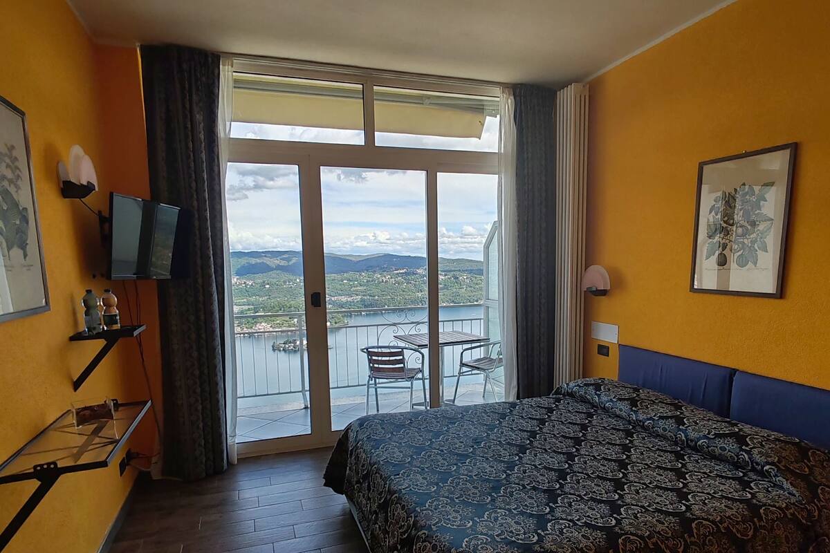 Ein Hotelzimmer mit einem großen Bett, einem Balkon mit Tisch und Stühlen und einem schönen Blick auf Stadt und Berge.