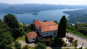 A large house with a red-tiled roof, surrounded by lush greenery and a lake. - Hotel Panoramico lago d'Orta adults only (Madonna del Sasso)