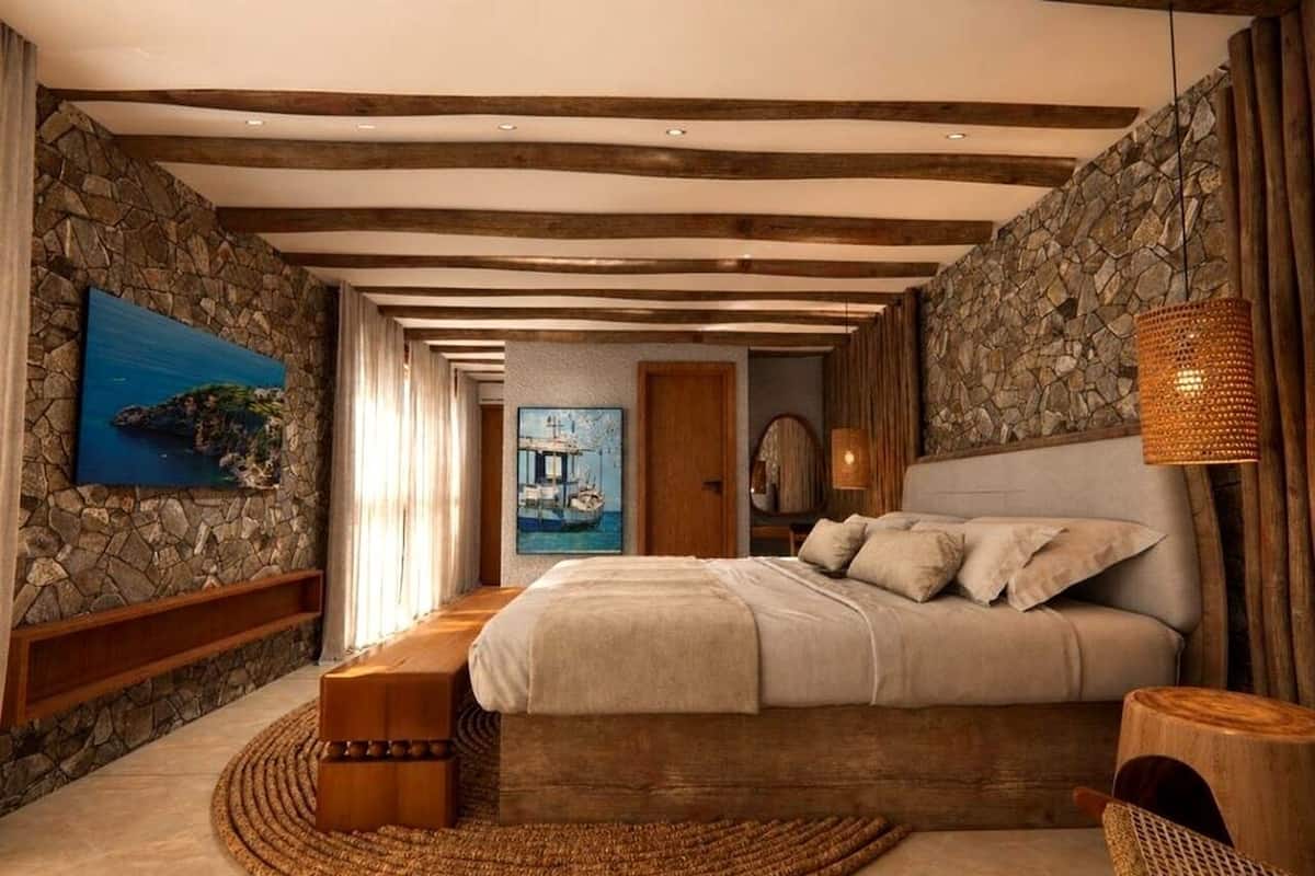 Een slaapkamer met een stenen muur, houten balken, een bed, een nachtkastje en een geweven vloerkleed.
