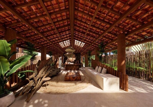 A covered outdoor area with a central seating area, wooden pillars, and a bamboo fence.