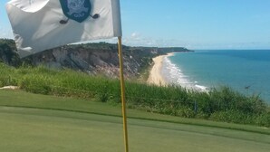 A golf flag on a flagpole with a view of a beach and ocean in the background. - Margaridas Boutique Hotel - antiga Pousada Jardim das Margaridas (Porto Seguro)