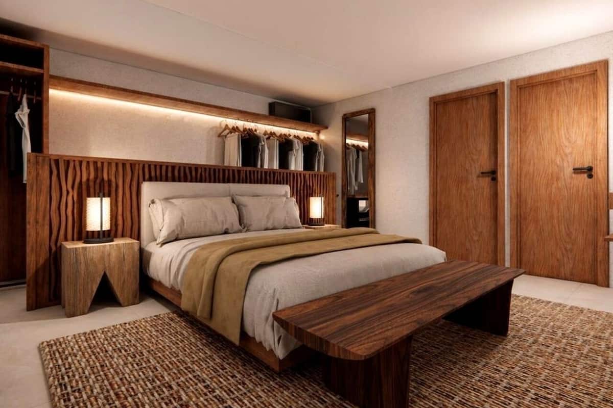 Een slaapkamer met een houten bed, nachtlampen, een houten bankje en een kledingkast.