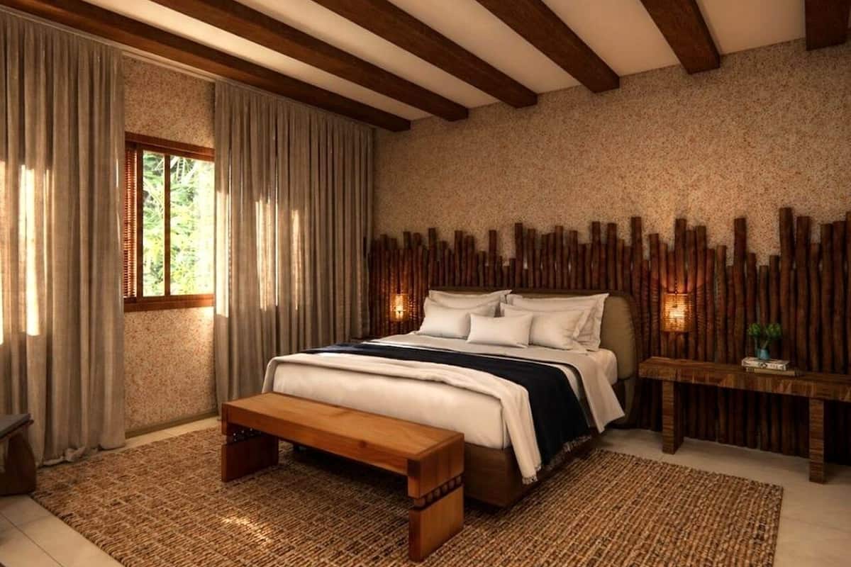 Slaapkamer met een groot bed, houten balken, een bankje, een nachtkastje en een wand met verticale houten latten.