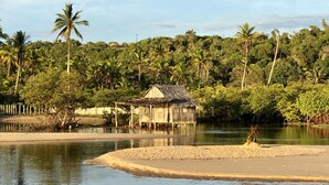 A wooden hut by a calm water body, surrounded by dense greenery and palm trees. - Margaridas Boutique Hotel - antiga Pousada Jardim das Margaridas (Porto Seguro)