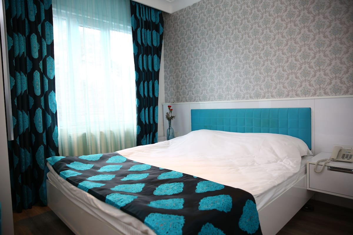 A hotel room with a bed, a nightstand, a telephone, and a window with curtains.